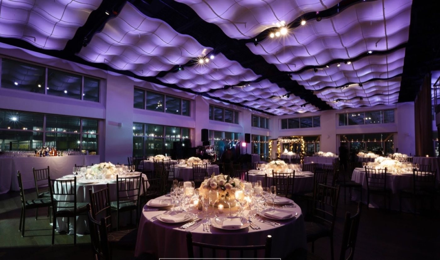 Waterfront event room set with round dinner tables under a wave-shaped lit ceiling