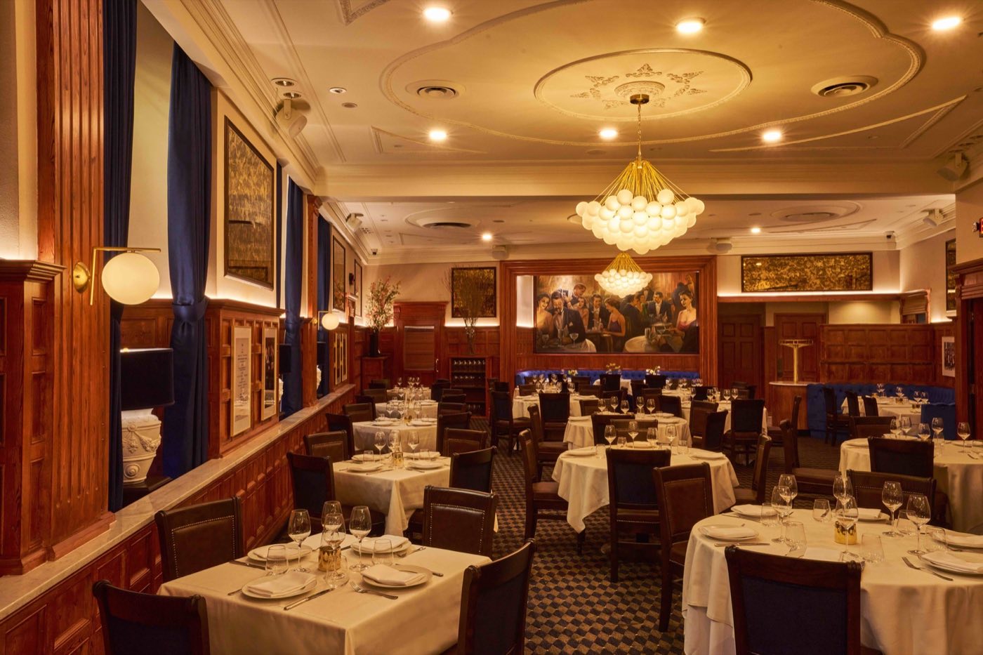 Dining room with mahogany paneling, crystal chandeliers and round tables set in white linen