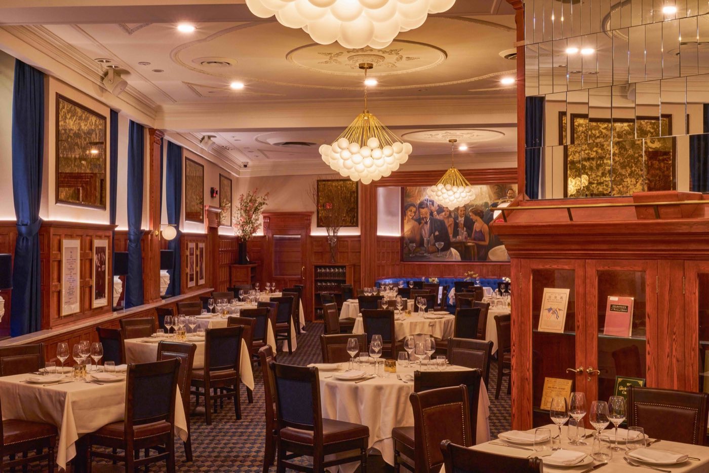 Long view of a paneled dining room with blue drapes, chandeliers and set tables