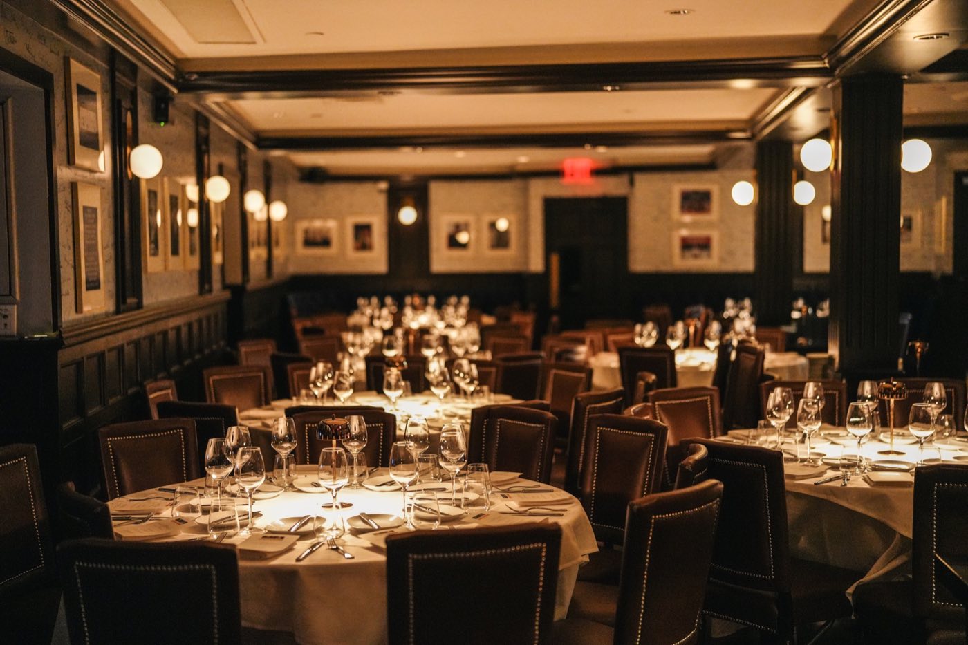Private dining room with framed pictures, leather chairs and round tables set for dinner
