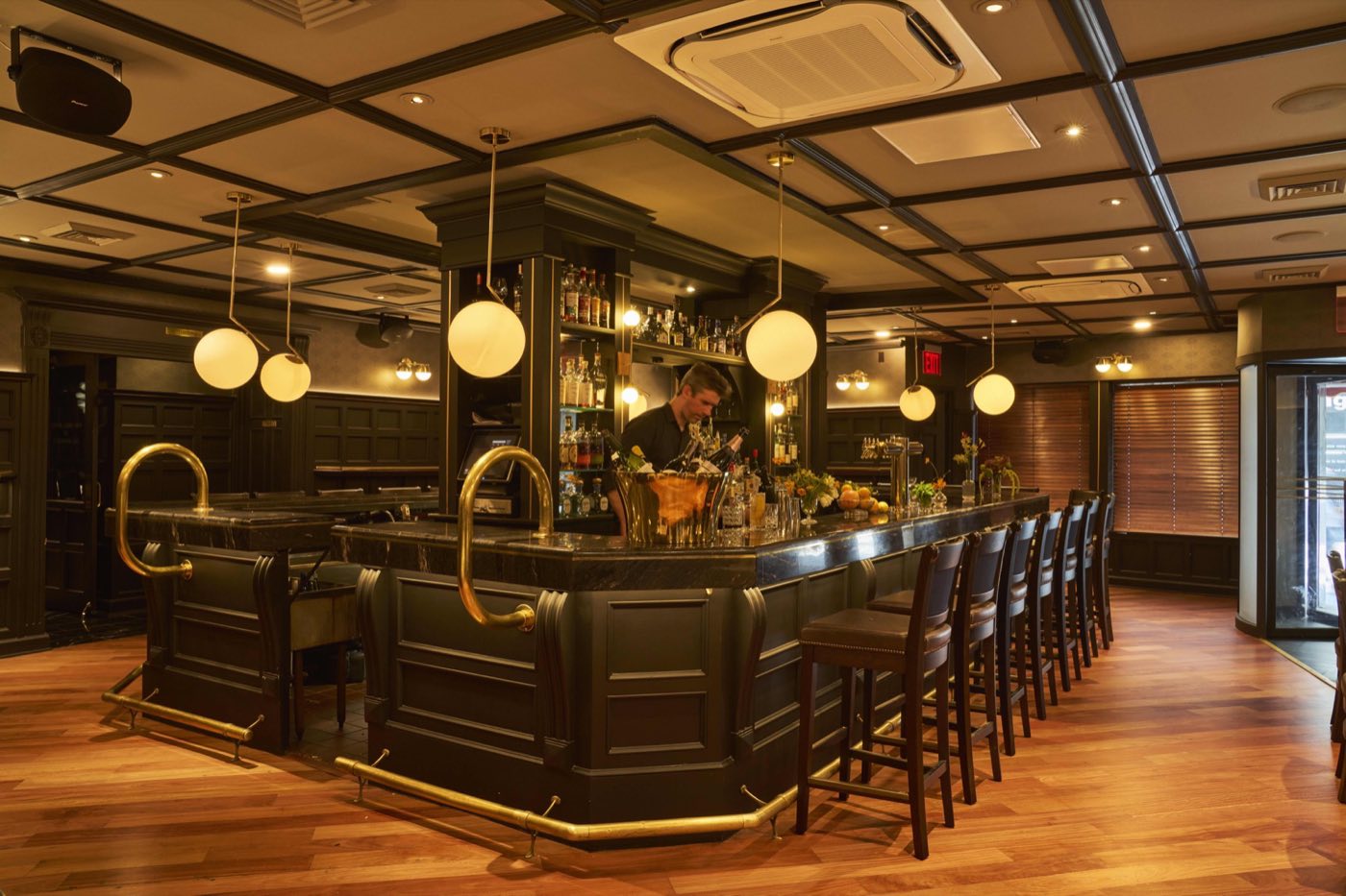 Dark wood bar with brass rails, globe pendant lights and a row of stools