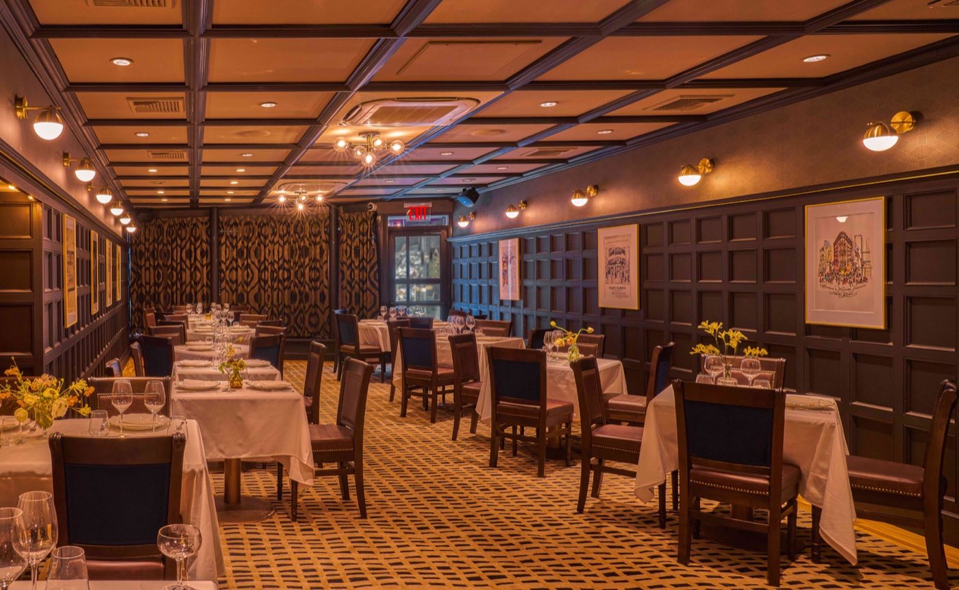 Paneled private room with coffered ceiling, patterned carpet and tables set with flowers