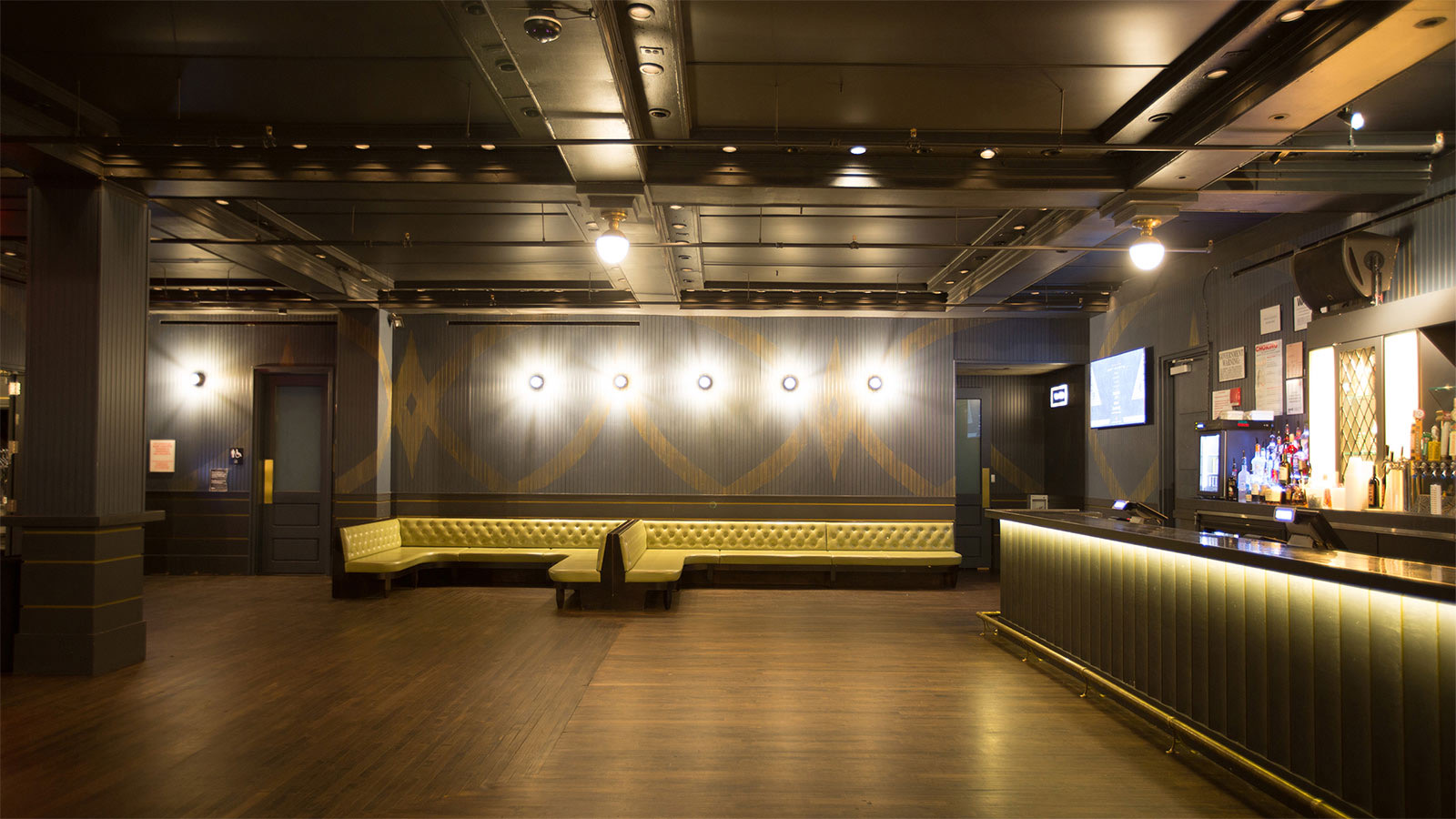 Empty lounge room with tufted banquettes, wood floor and a long backlit bar