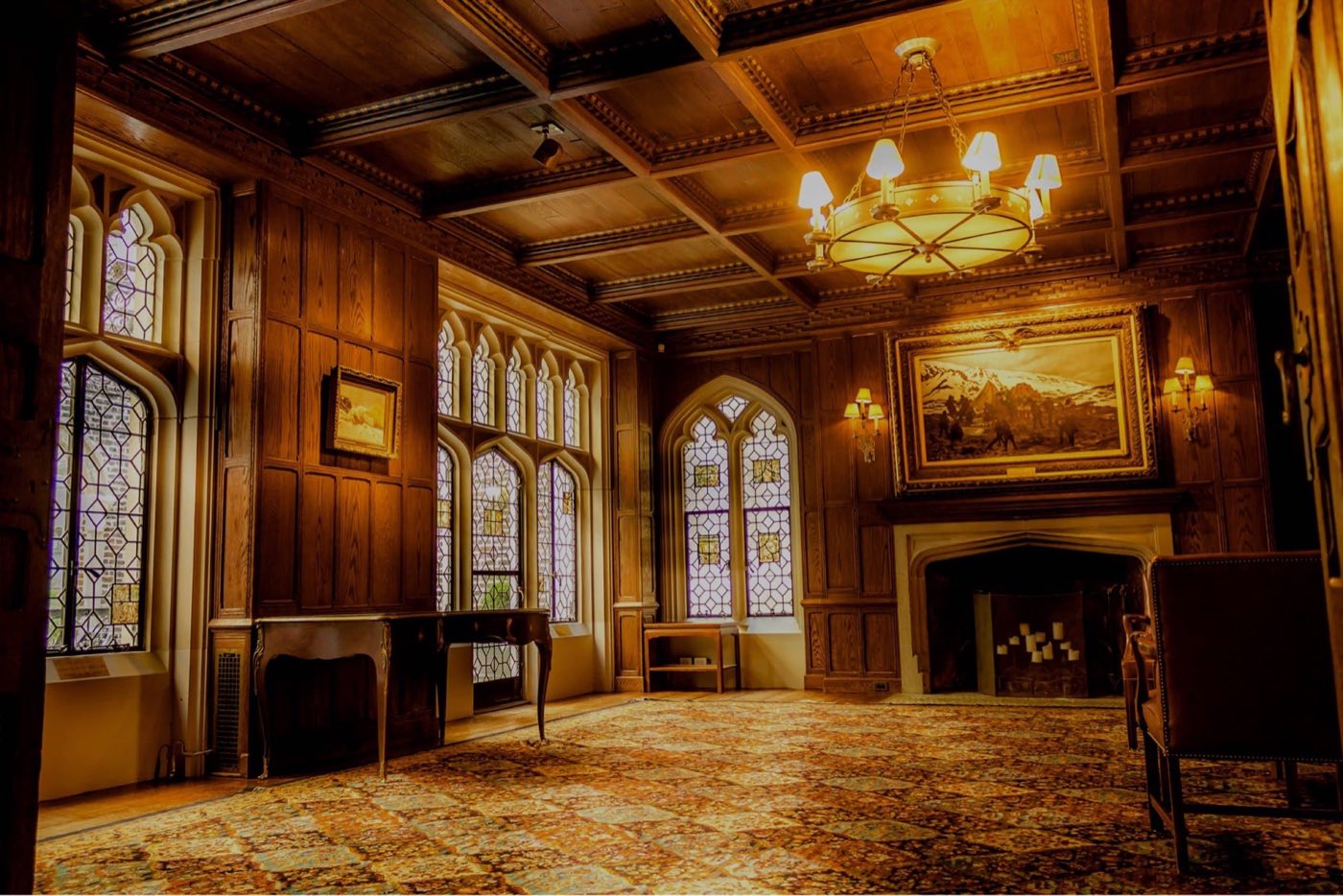 Wood-paneled library with a coffered ceiling, stained glass windows and a fireplace