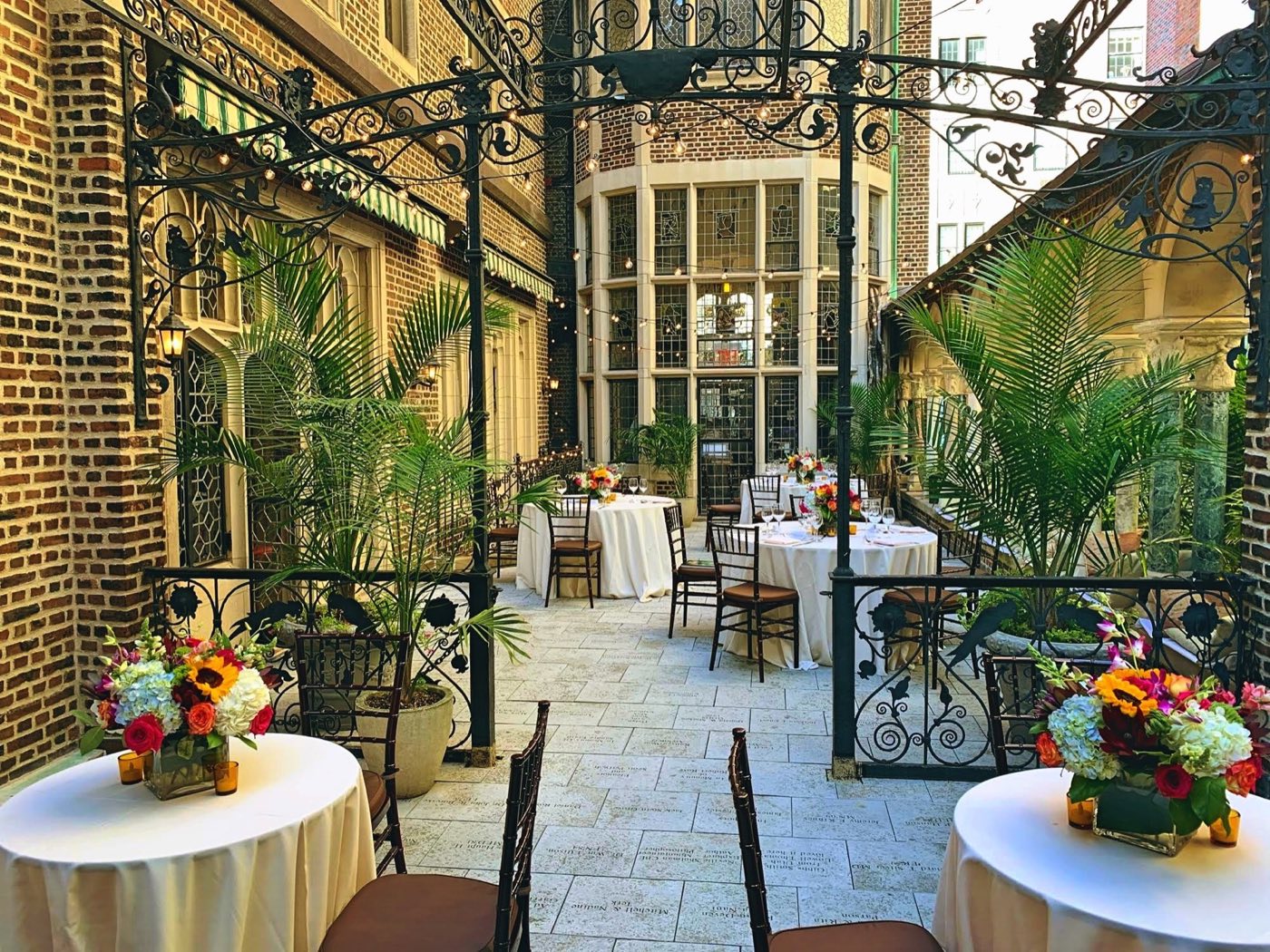 Second-floor terrace with iron trellis, palms and round tables set for dinner