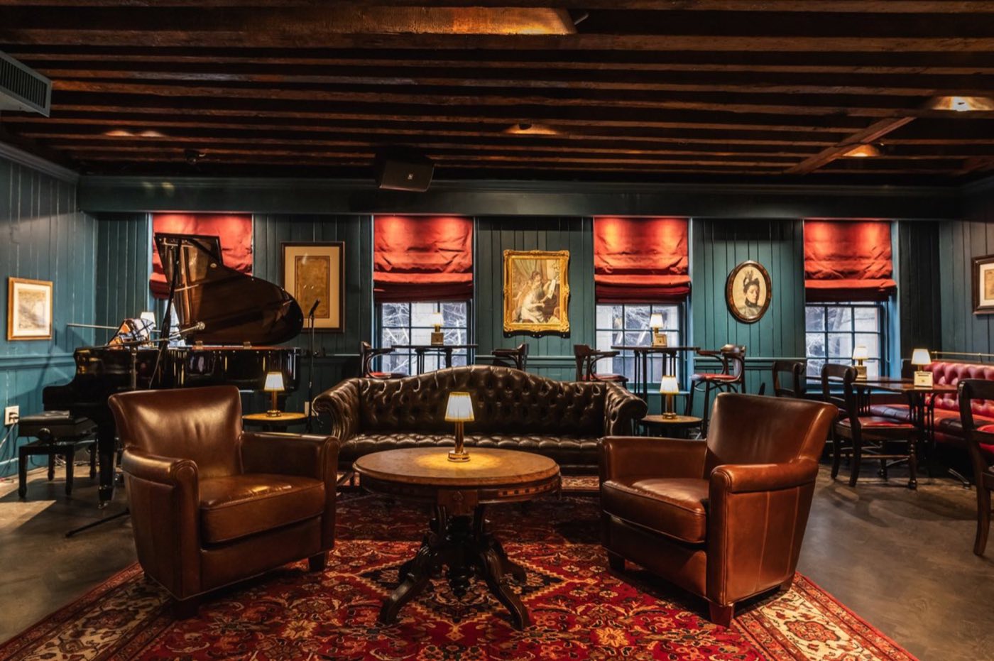 Upstairs piano bar with a grand piano, leather armchairs and red window shades