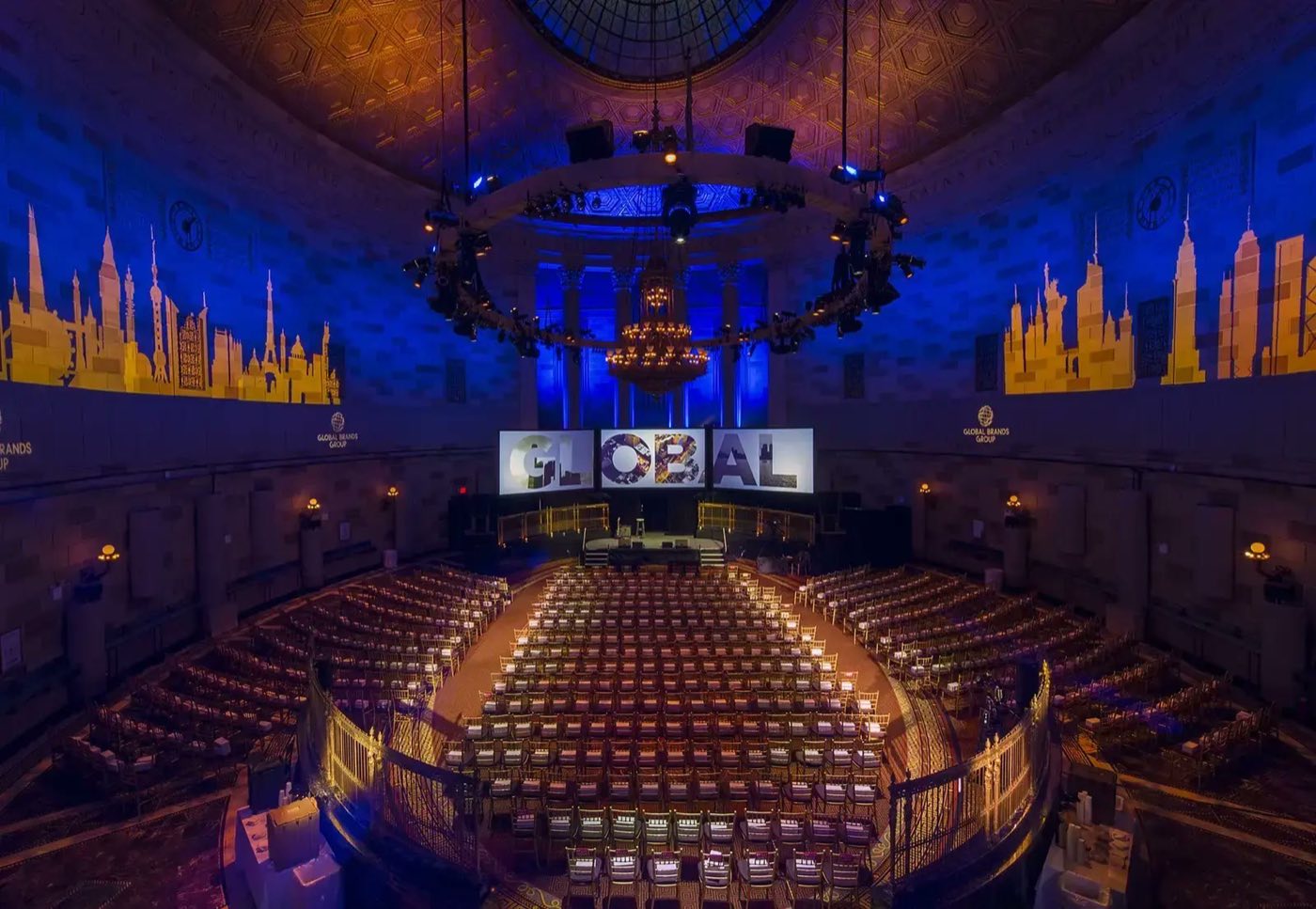 Ballroom in theater seating facing a stage with city skyline set pieces