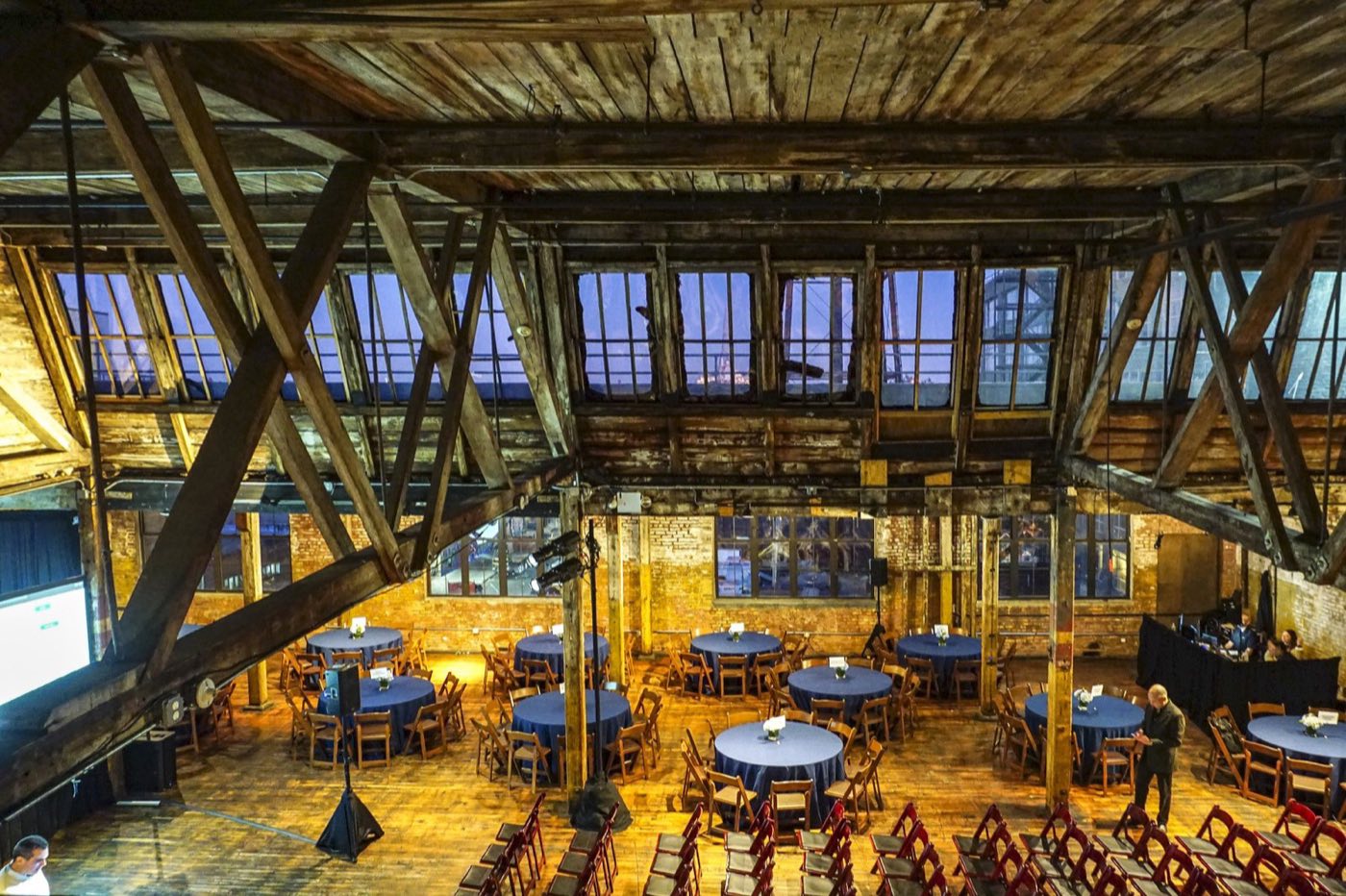 Timber-truss loft set with round tables under the sawtooth skylights