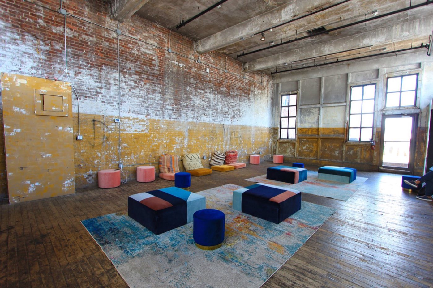 Brick-walled loft room with blue ottomans and rugs on a wood floor