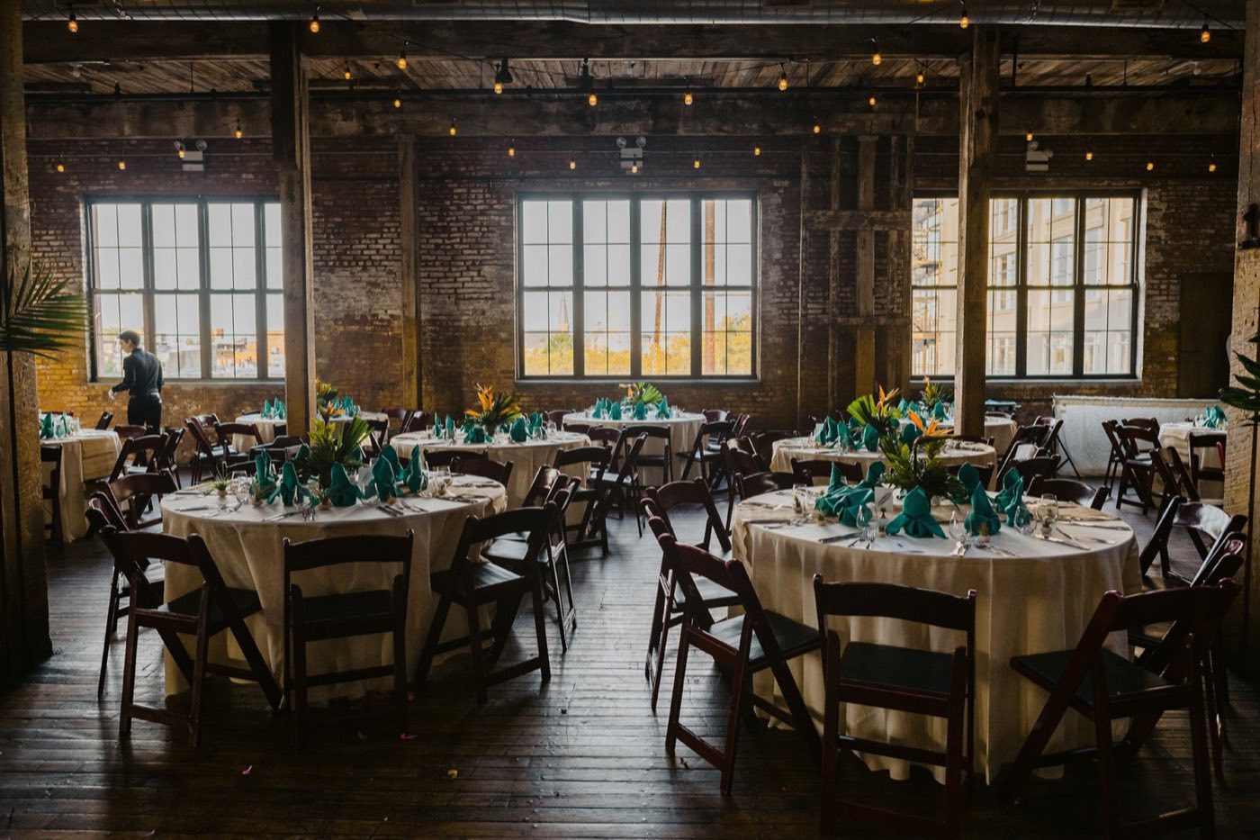 Round dinner tables beneath tall factory windows and exposed brick