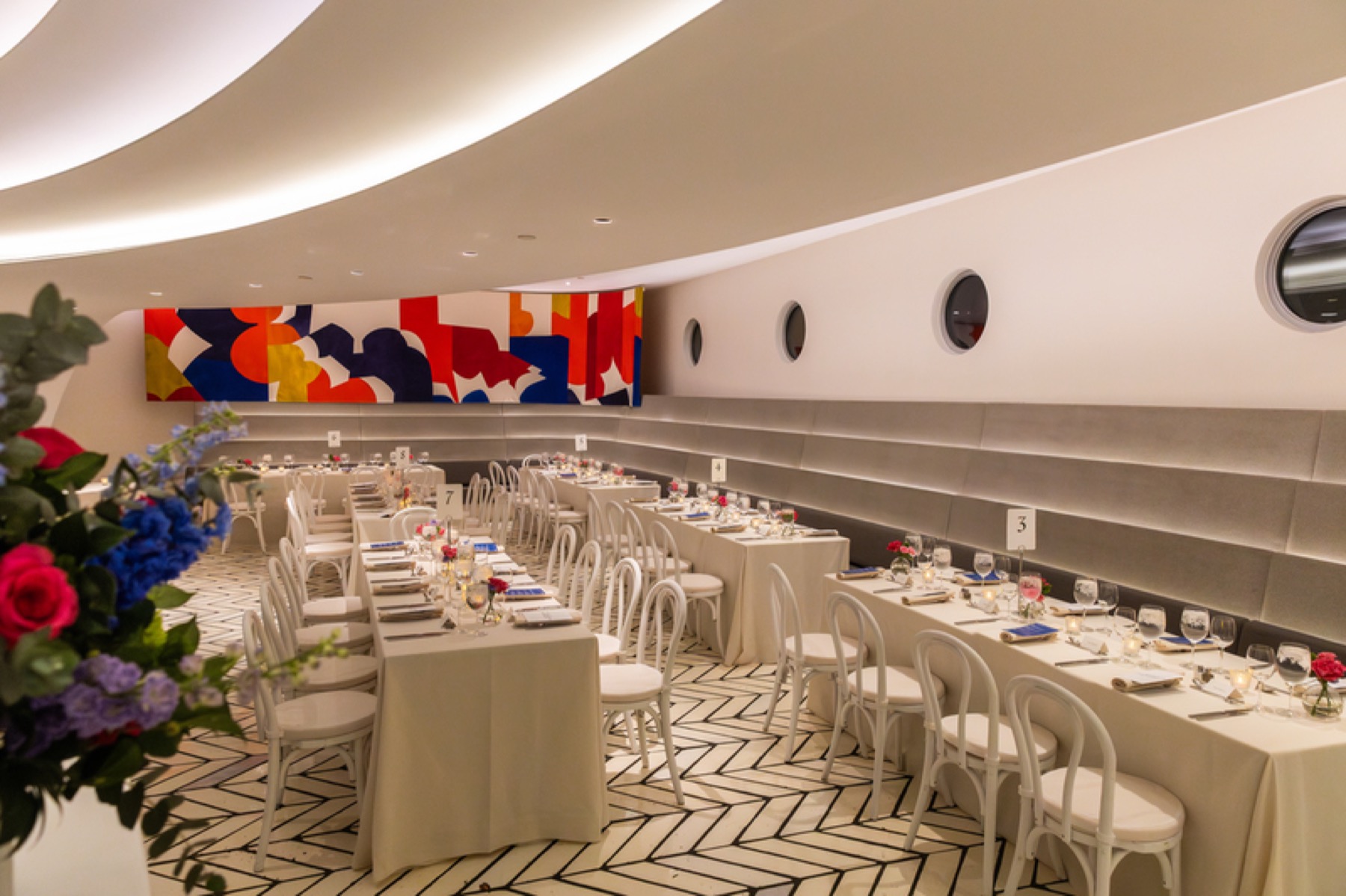 Long dinner tables set in a curved room with an abstract mural