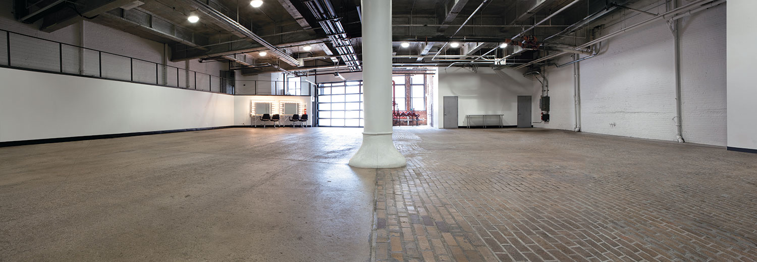Empty ground floor stage with cobblestone floor, white brick walls and garage door