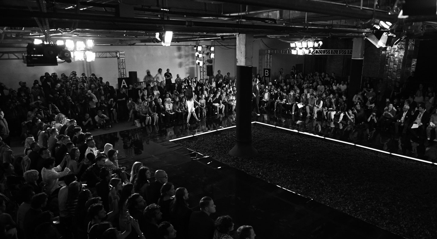 Lit runway surrounded by tiered seating in a dark industrial stage