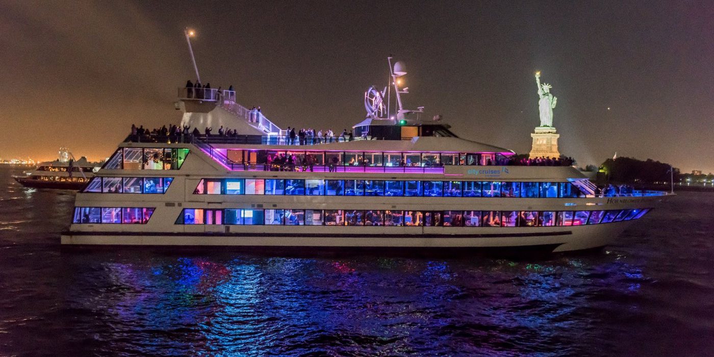 The yacht lit up at night on the harbor near the Statue of Liberty