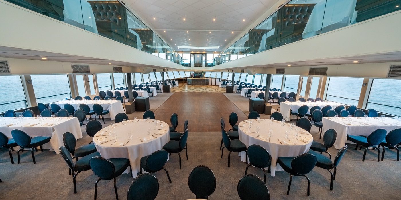 Upper deck interior set with round tables and harbor views