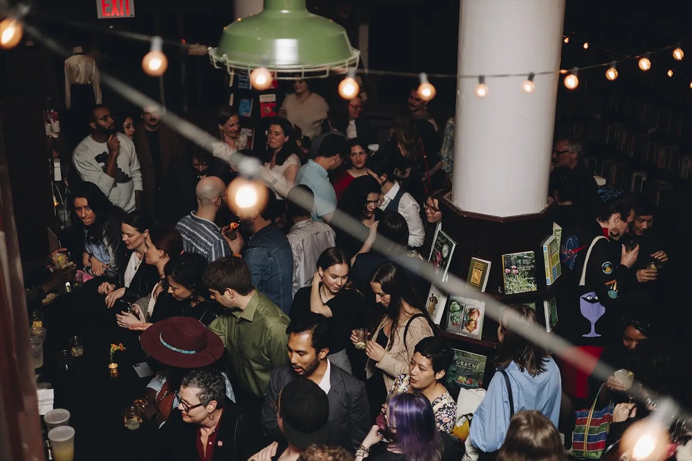 Crowded evening reception under string lights between book-lined columns
