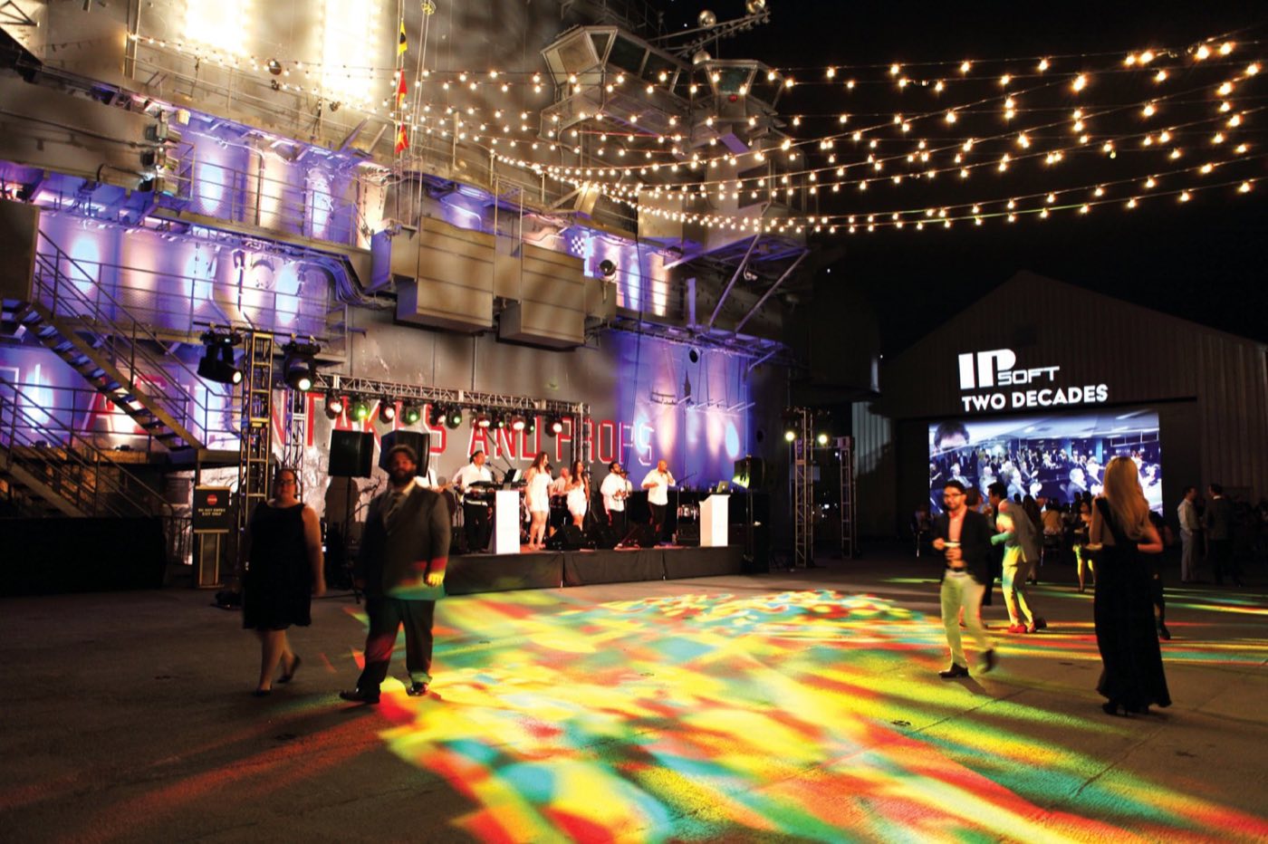 Night party on the flight deck with string lights, a stage and a lit dance floor