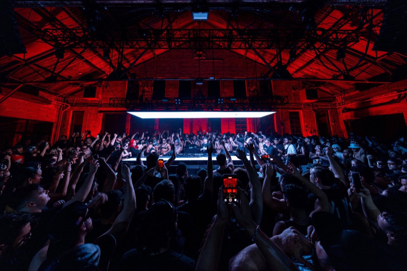 Main hall with a centered stage and red-lit steel roof trusses above the crowd