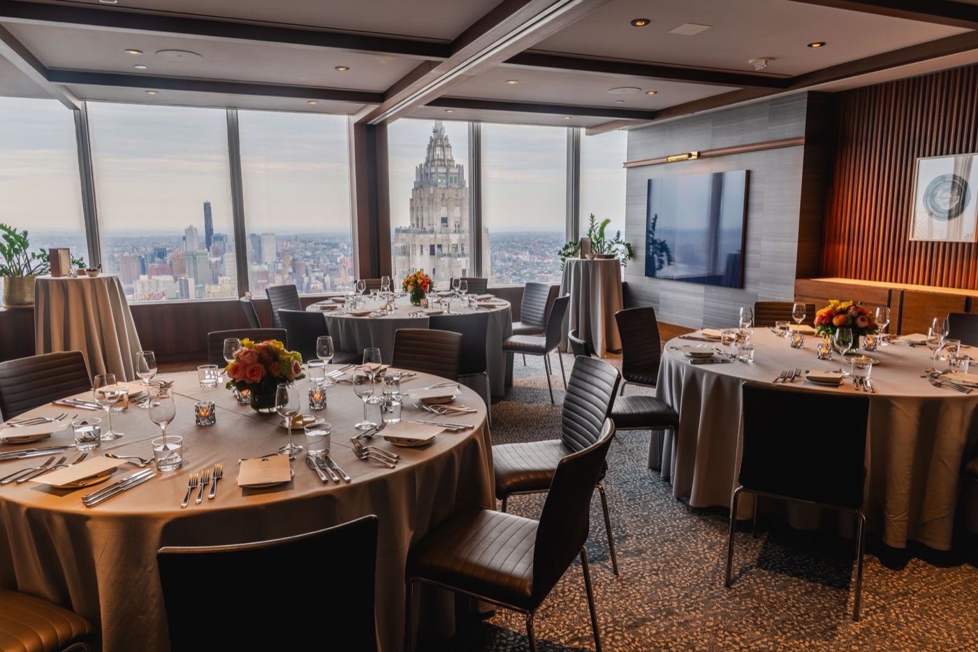 Corner dining room with round tables and a skyline view through tall windows