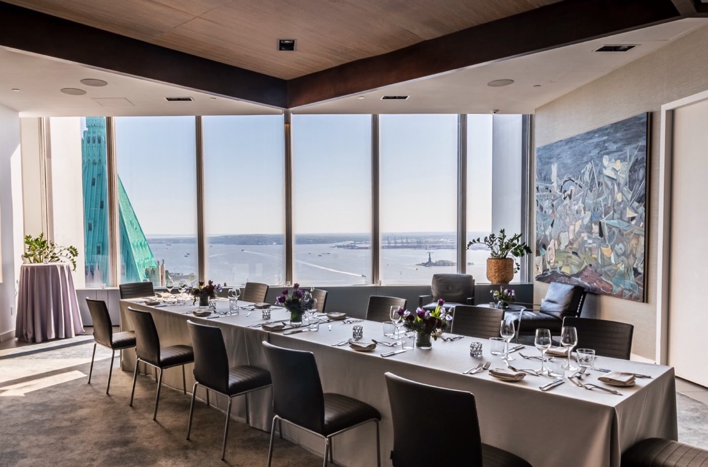 Long dinner table set in a private room with windows facing New York Harbor