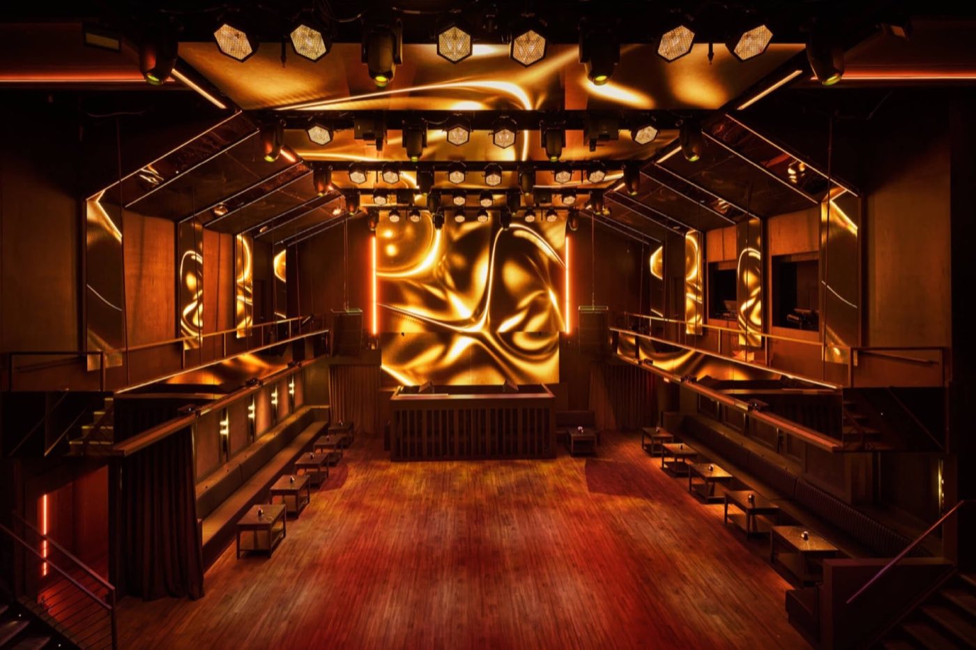 Main room lit in amber with a gold LED backdrop, bottle-service booths and dance floor