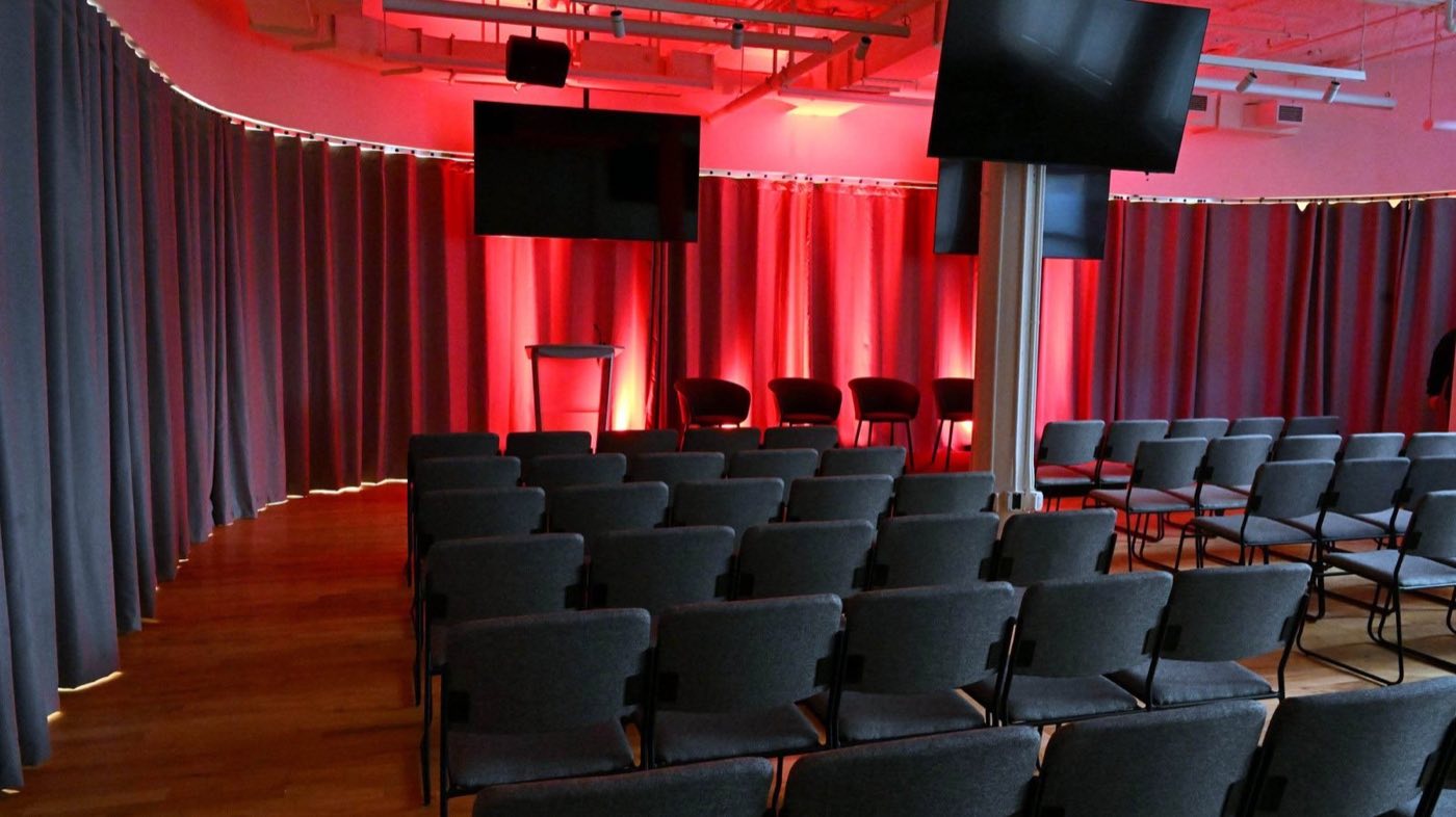 Theater-style rows of chairs facing screens with red curtain lighting