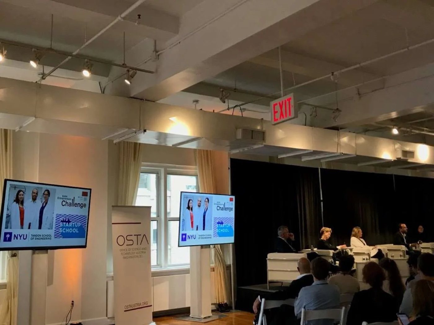 Panel discussion in the loft with screens and a seated audience