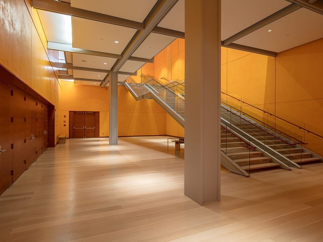 Warm orange lobby with pale wood floors, steel columns and a glass railed staircase
