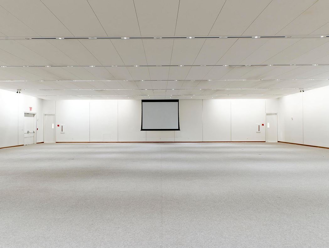 Large empty white conference hall with carpeted floor and a drop down projection screen