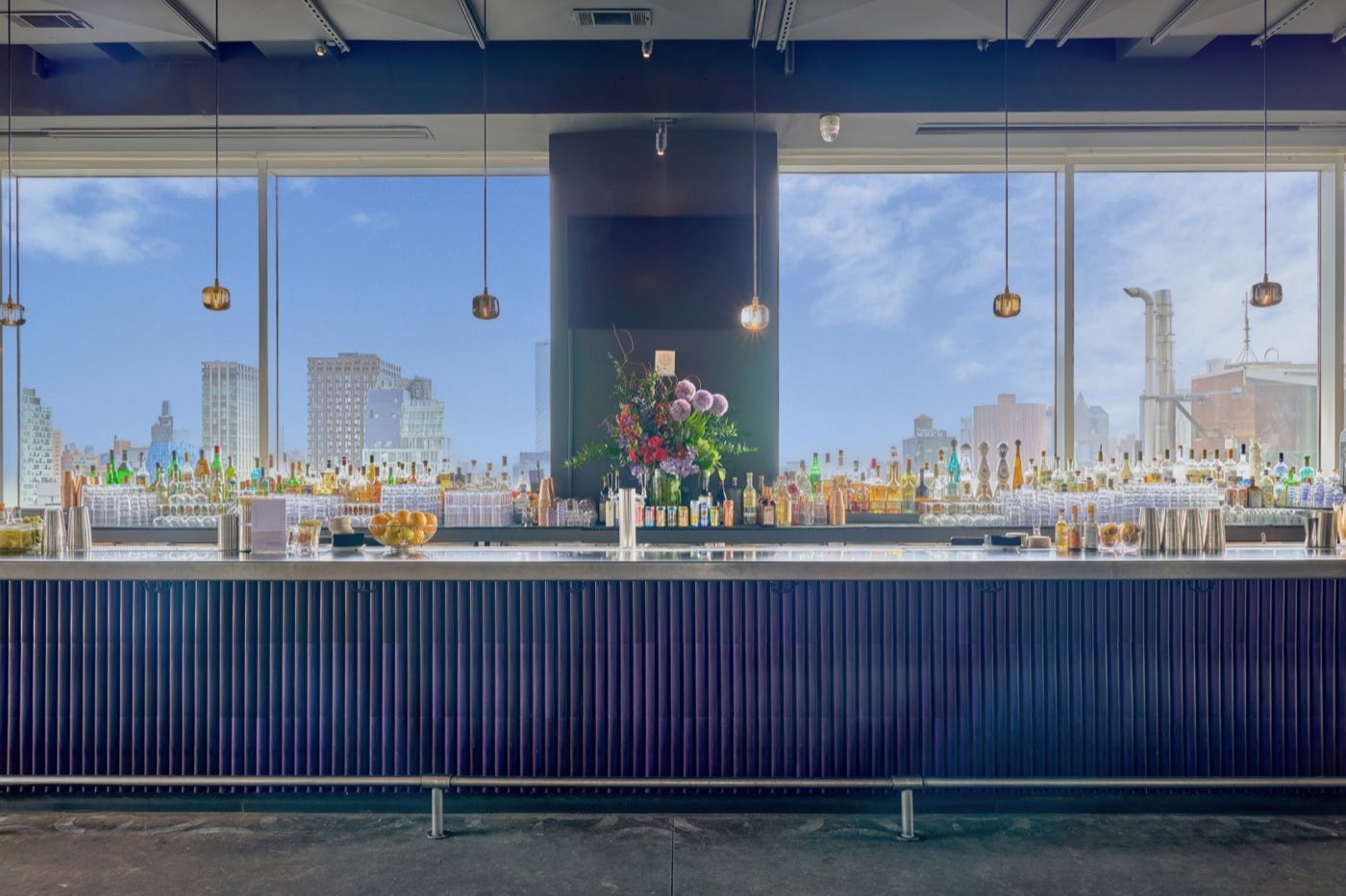 Long indoor bar with glass walls behind it and a view over downtown rooftops