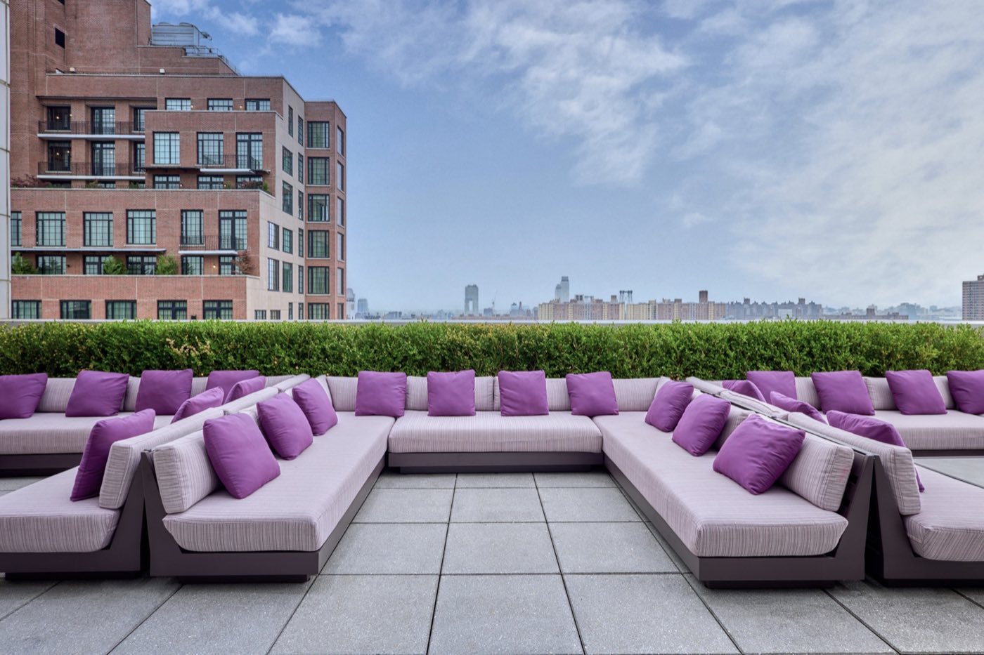 Terrace lounge with long sectional sofas, purple cushions and a hedge along the edge
