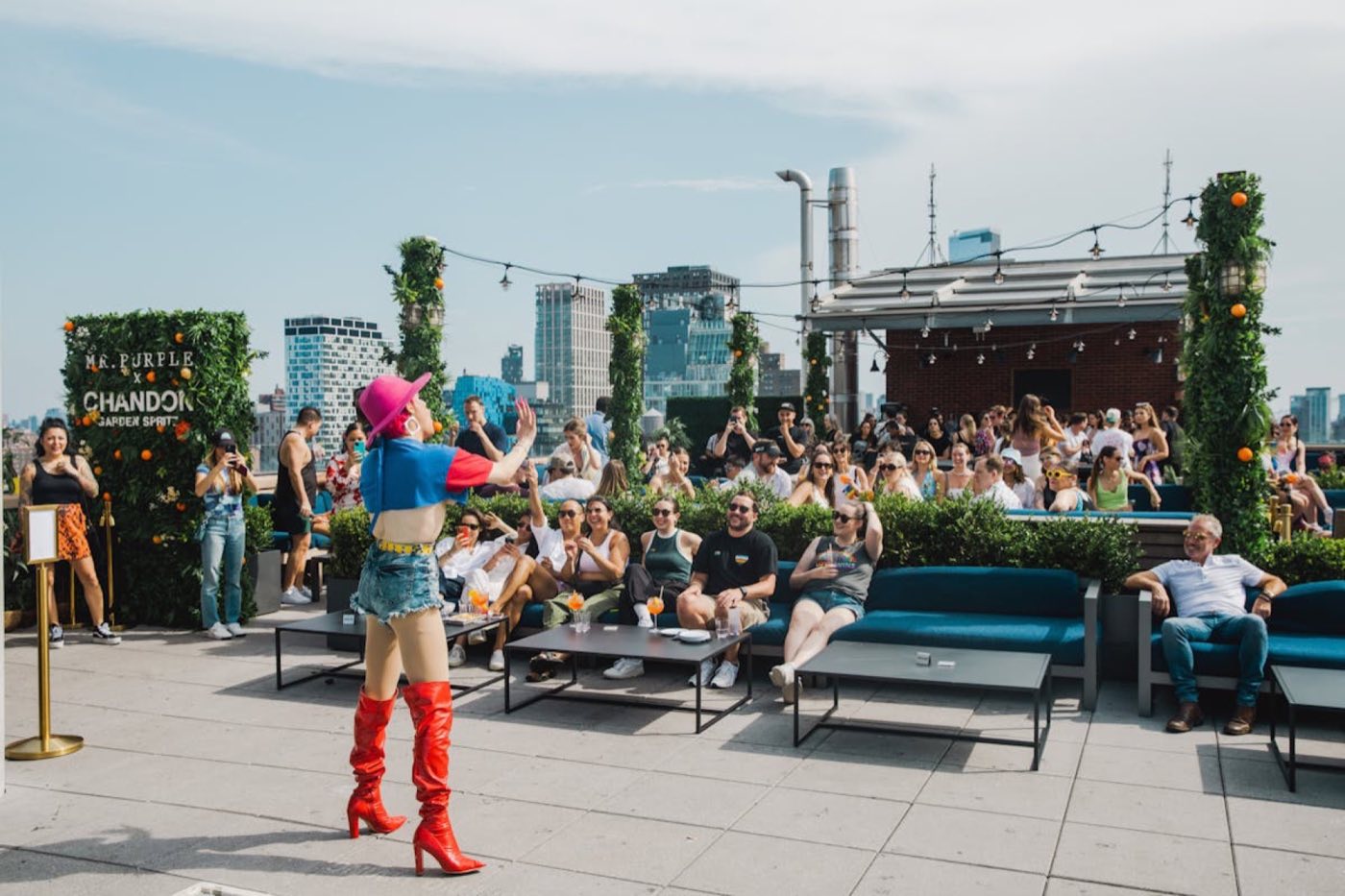 Daytime rooftop event with a performer, lounge seating and a crowd on the terrace