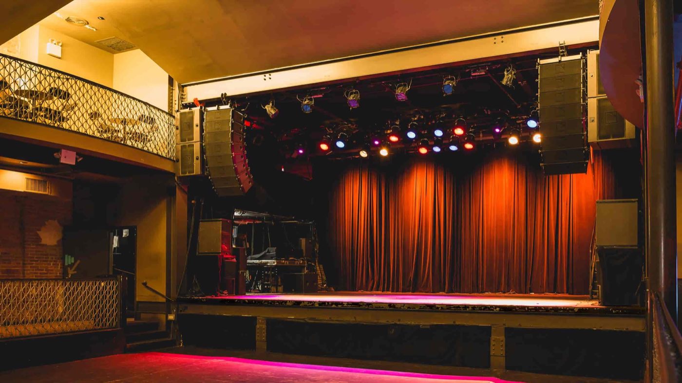 Main floor of the concert hall facing a curtained stage with speaker stacks and lights