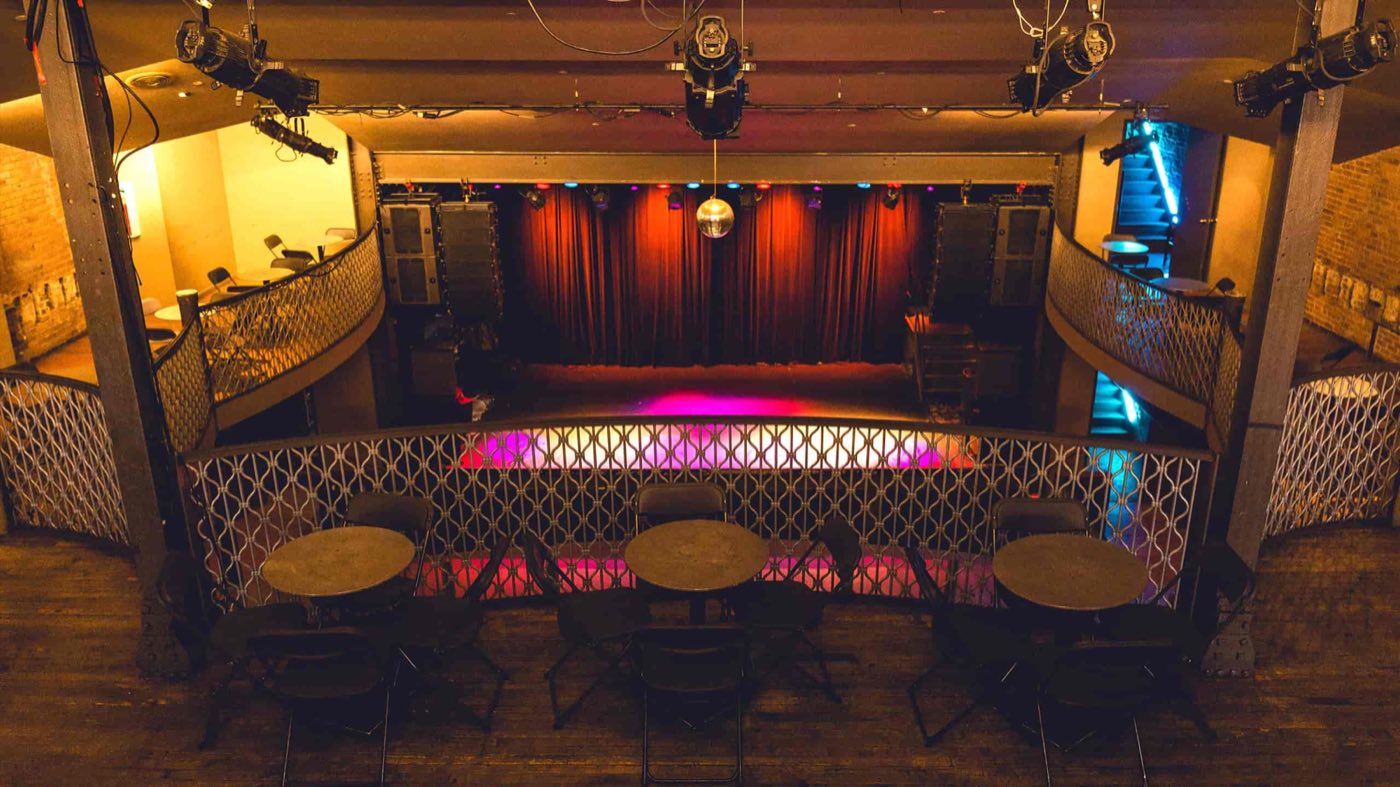 Balcony with cafe tables looking down over the main floor toward the stage