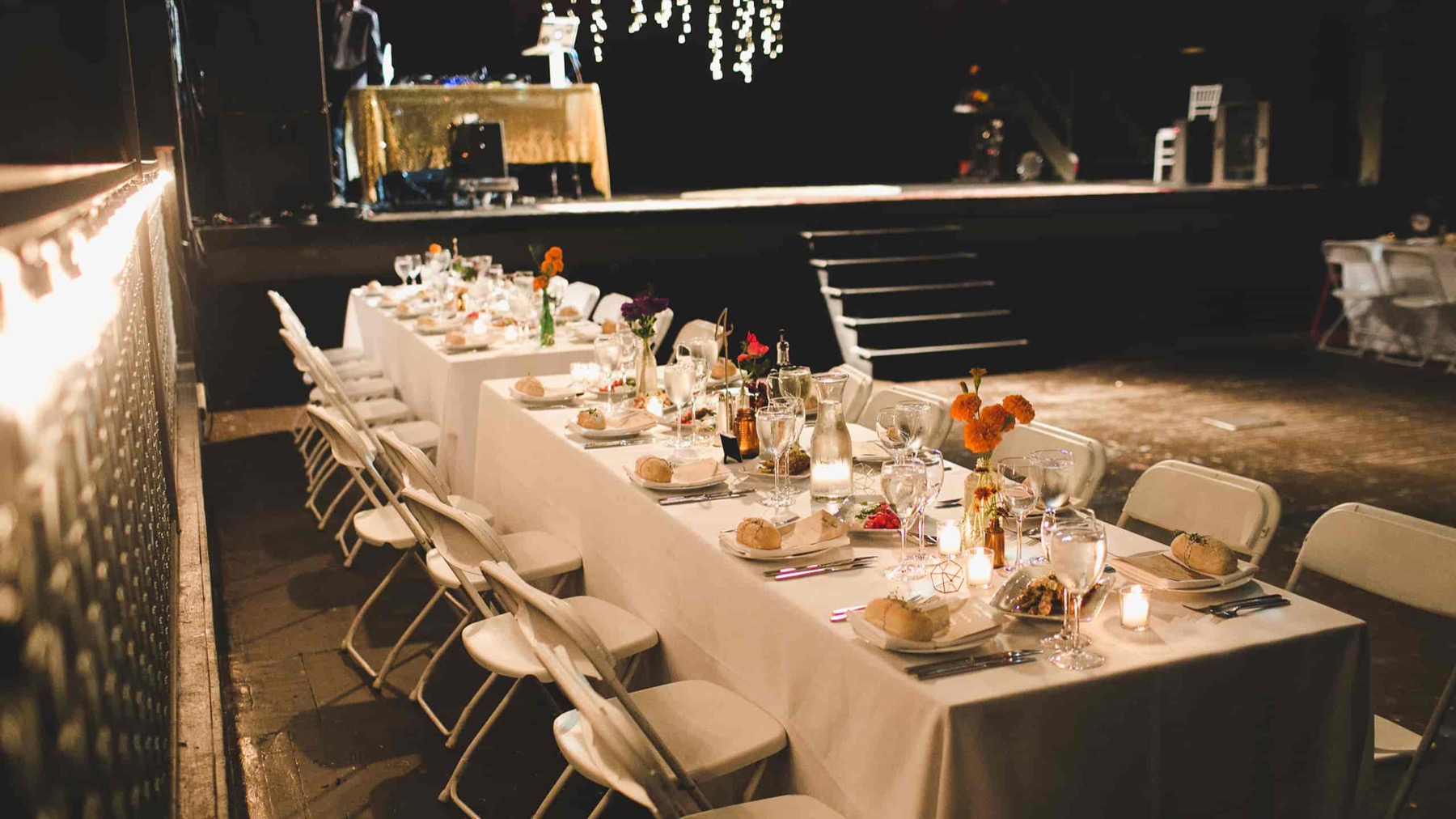 Long dinner table with white linens and candles set in front of the stage