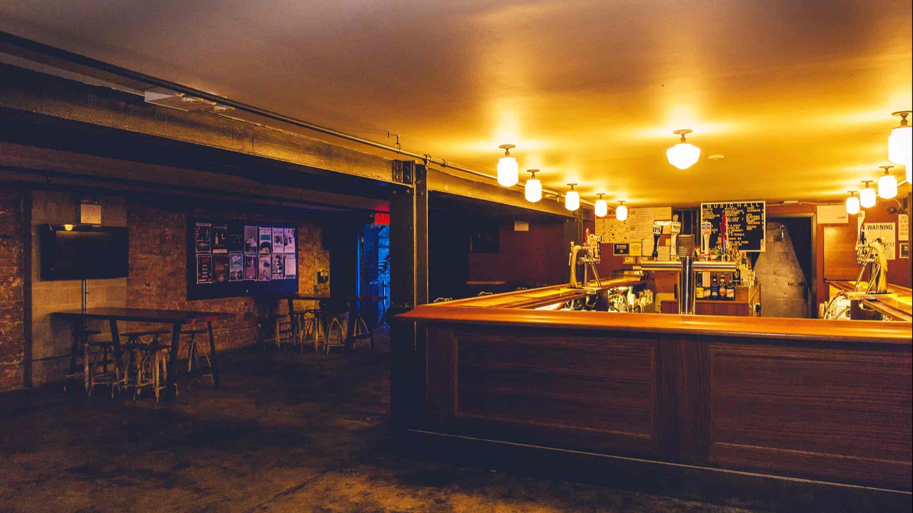 Lower-level lounge with a long wood bar, brick walls and warm pendant lights