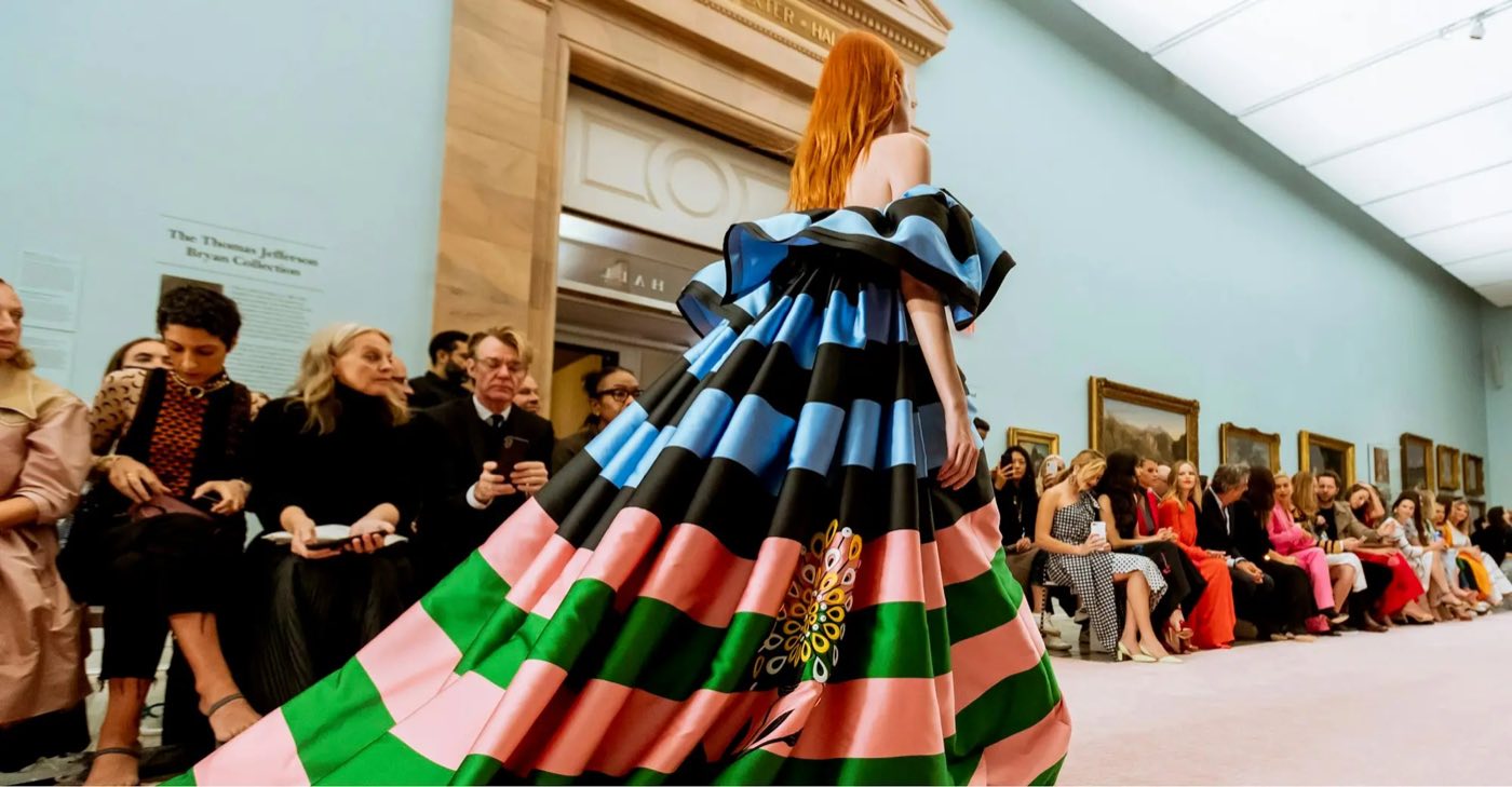 Runway show in a long picture gallery with guests seated on both sides