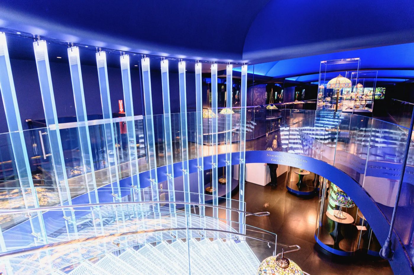 Two-level Tiffany lamp gallery with a lit glass staircase in blue light