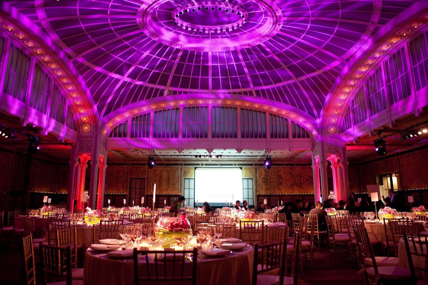 Celeste Bartos Forum set with round dinner tables under its glass dome, lit in magenta