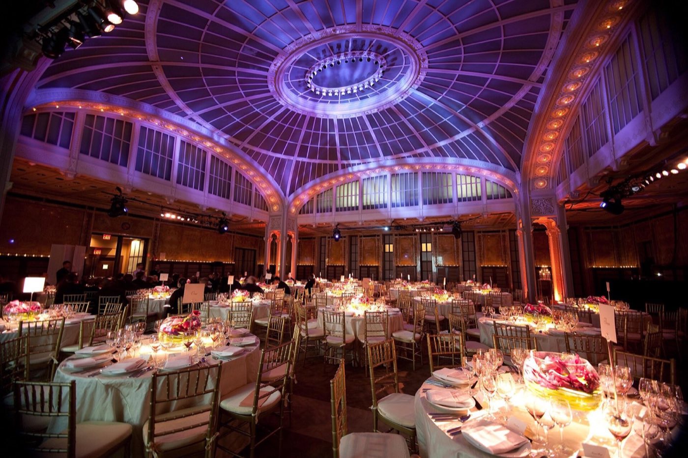 Round dinner tables with candles filling the forum beneath the arched glass ceiling