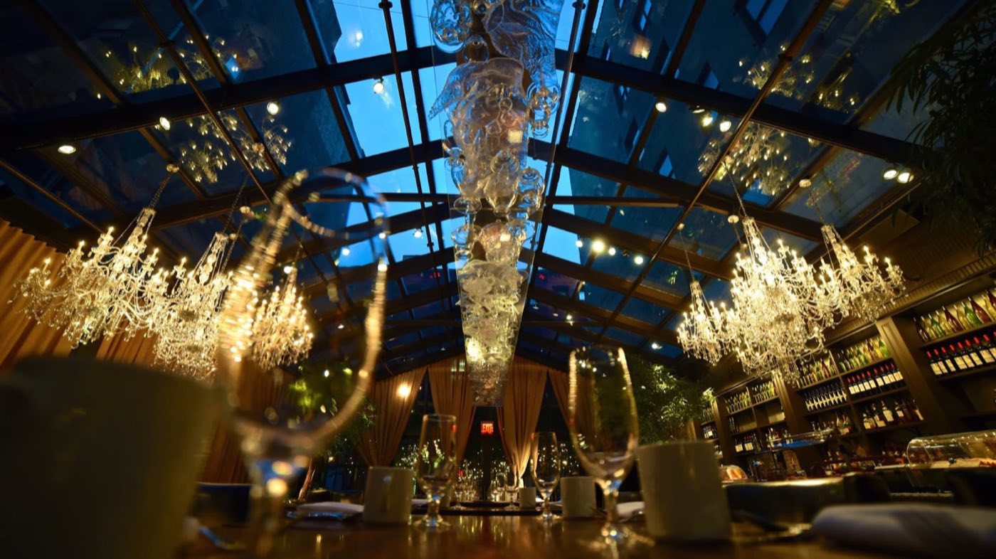 NoMo Kitchen at night under its glass roof with chandeliers and greenery