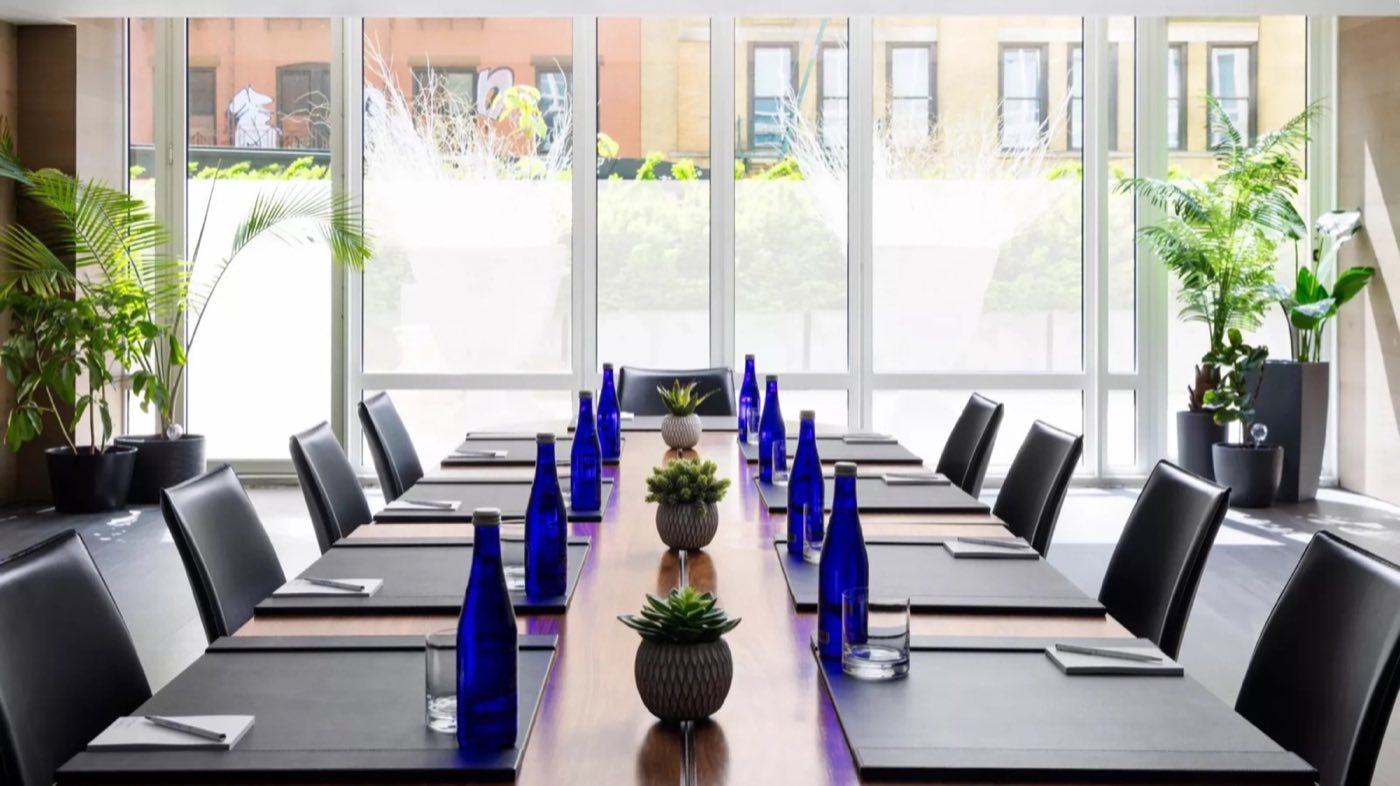 Glass-walled meeting room with a long boardroom table and potted plants