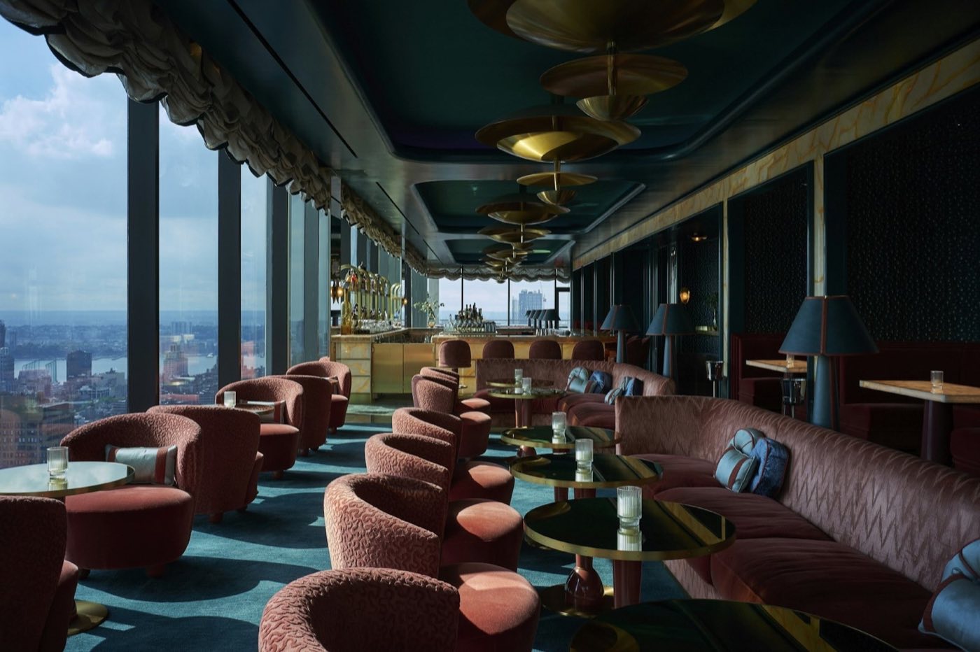 Lounge with curved velvet seating, teal carpet and tall windows over the city