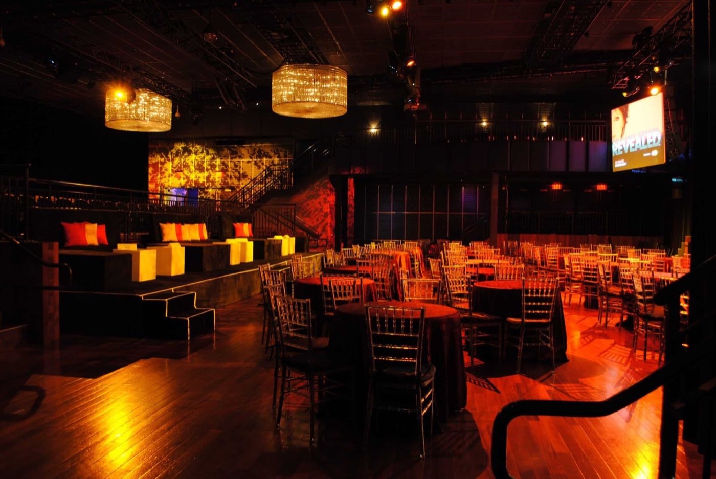 Venue set for a seated dinner with bar and chandeliers under warm light