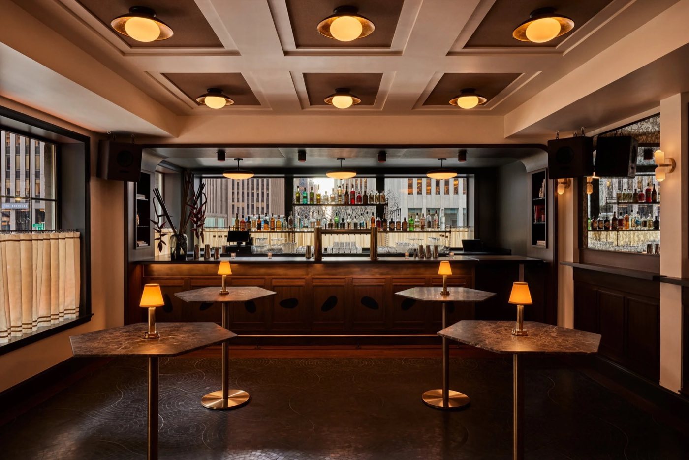 Second-floor bar with a coffered ceiling, cocktail tables and street-facing windows