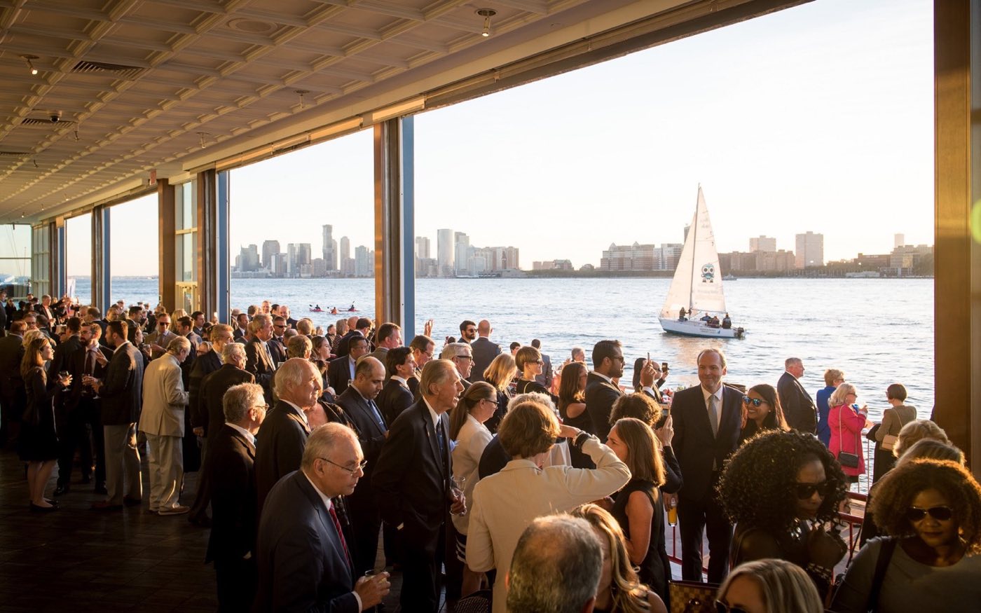 Guests at a reception inside the glass-walled room overlooking the Hudson River at sunset