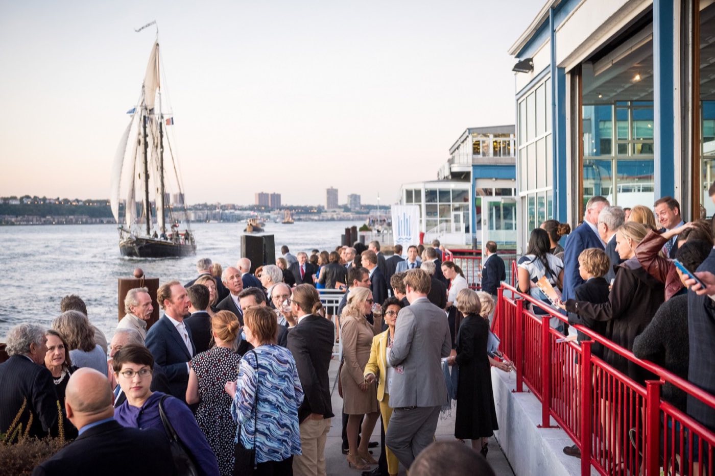 Evening reception on the pier deck with a tall ship passing on the river
