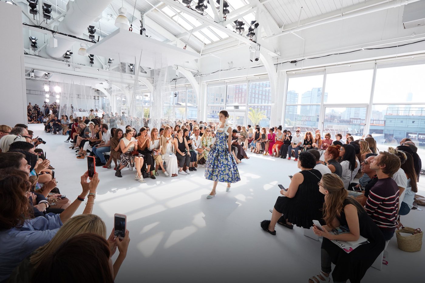 Runway show in a white skylit studio with guests seated along both sides