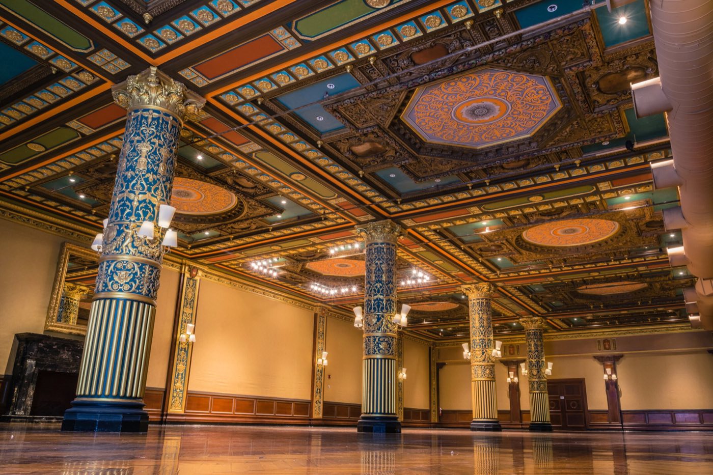 Empty ballroom with a painted coffered ceiling, gilded columns and polished wood floor