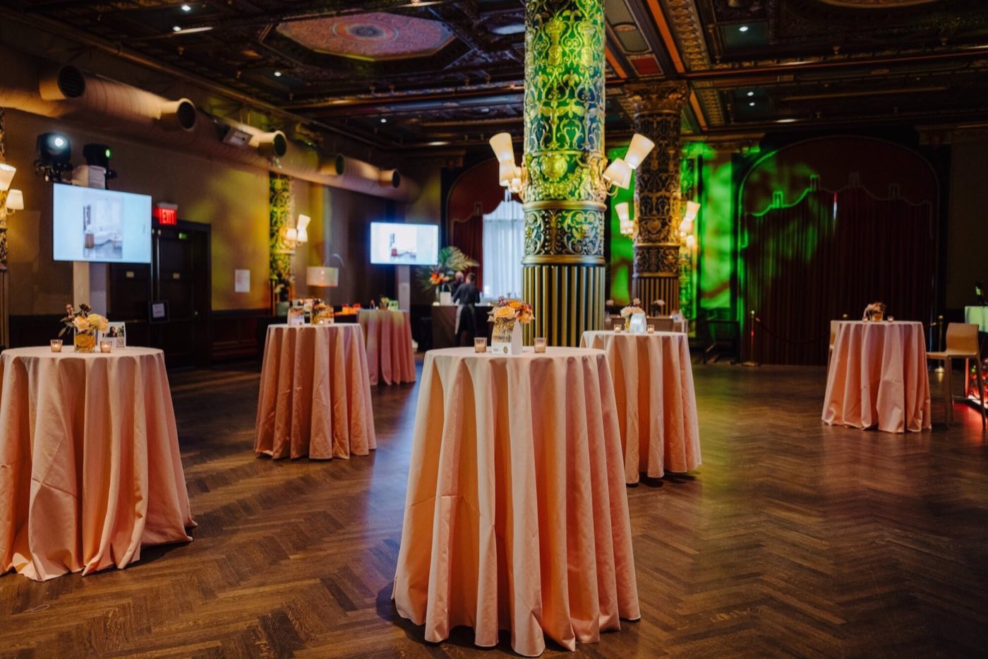 Ballroom set for a reception with high-top tables, screens and green uplighting
